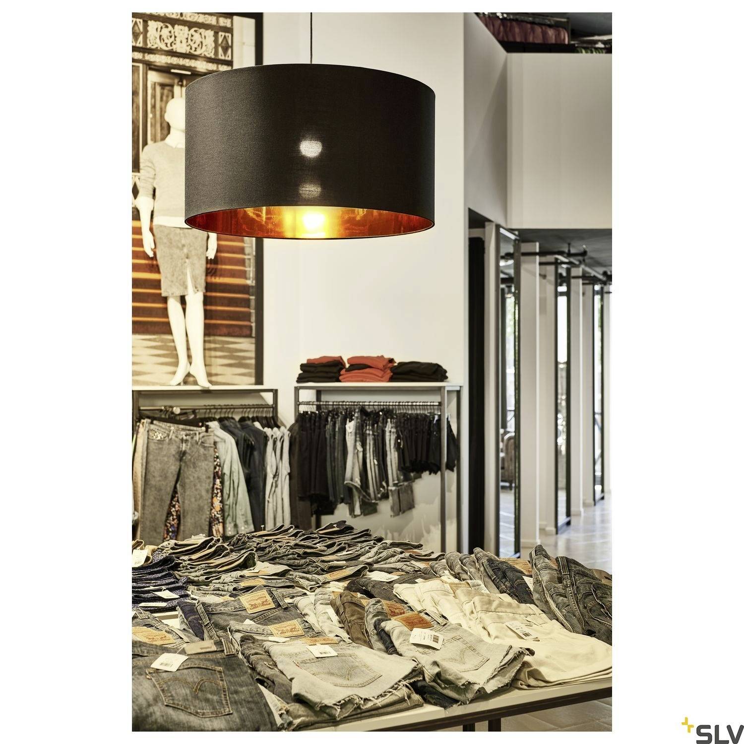 Clothing store with a table laden with folded jeans, above which hangs a large, black lampshade. Shelves are visible in the background.