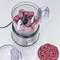 An electric meat grinder minces raw meat, visible in the transparent container. Beside it lies a bowl with chopped meat.