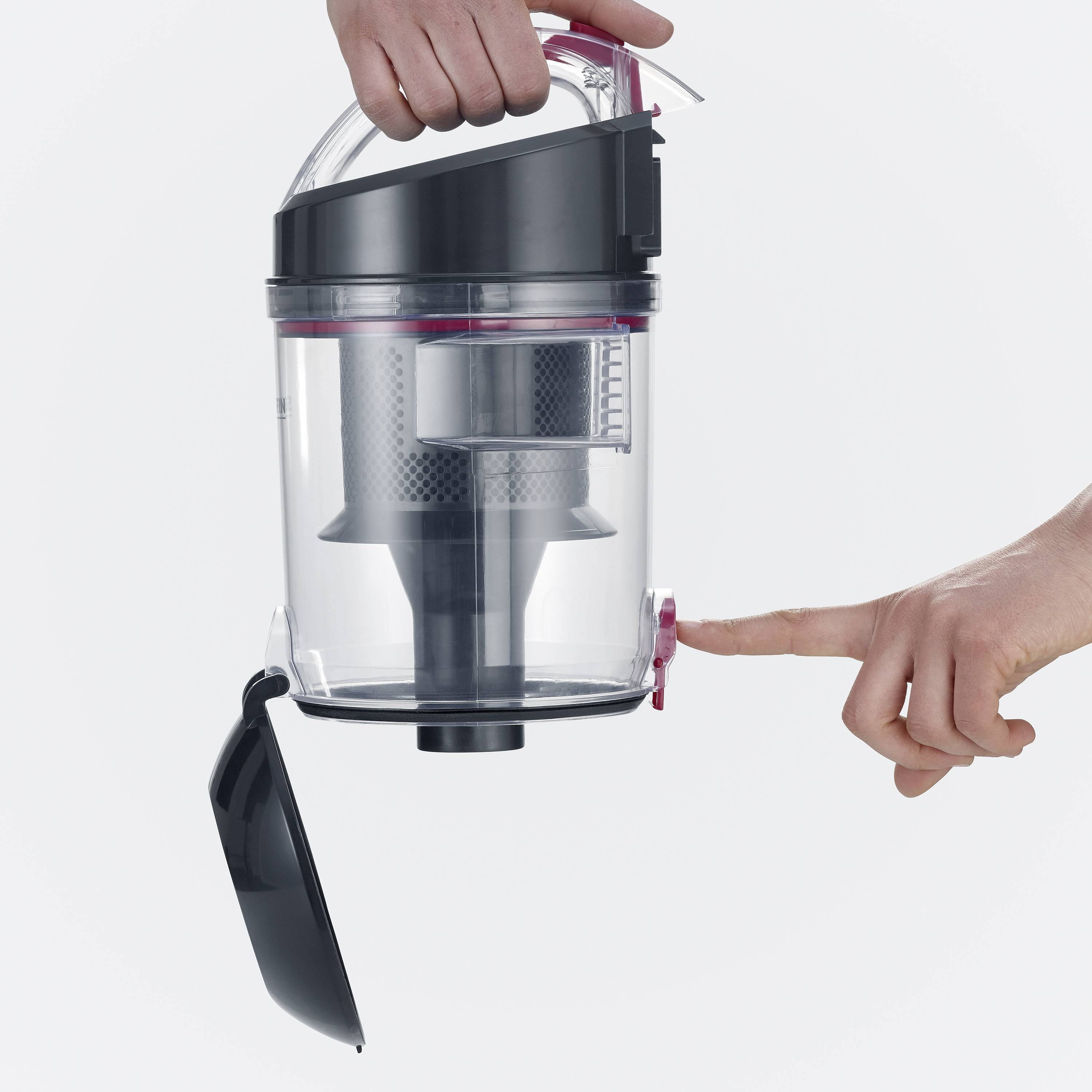 A vacuum cleaner container is being emptied. A hand presses a button to open the bottom lid and release the dirt.