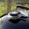 A closed kettle barbecue outdoors with a thermometer on the lid indicating the temperature. Grass is visible in the background.