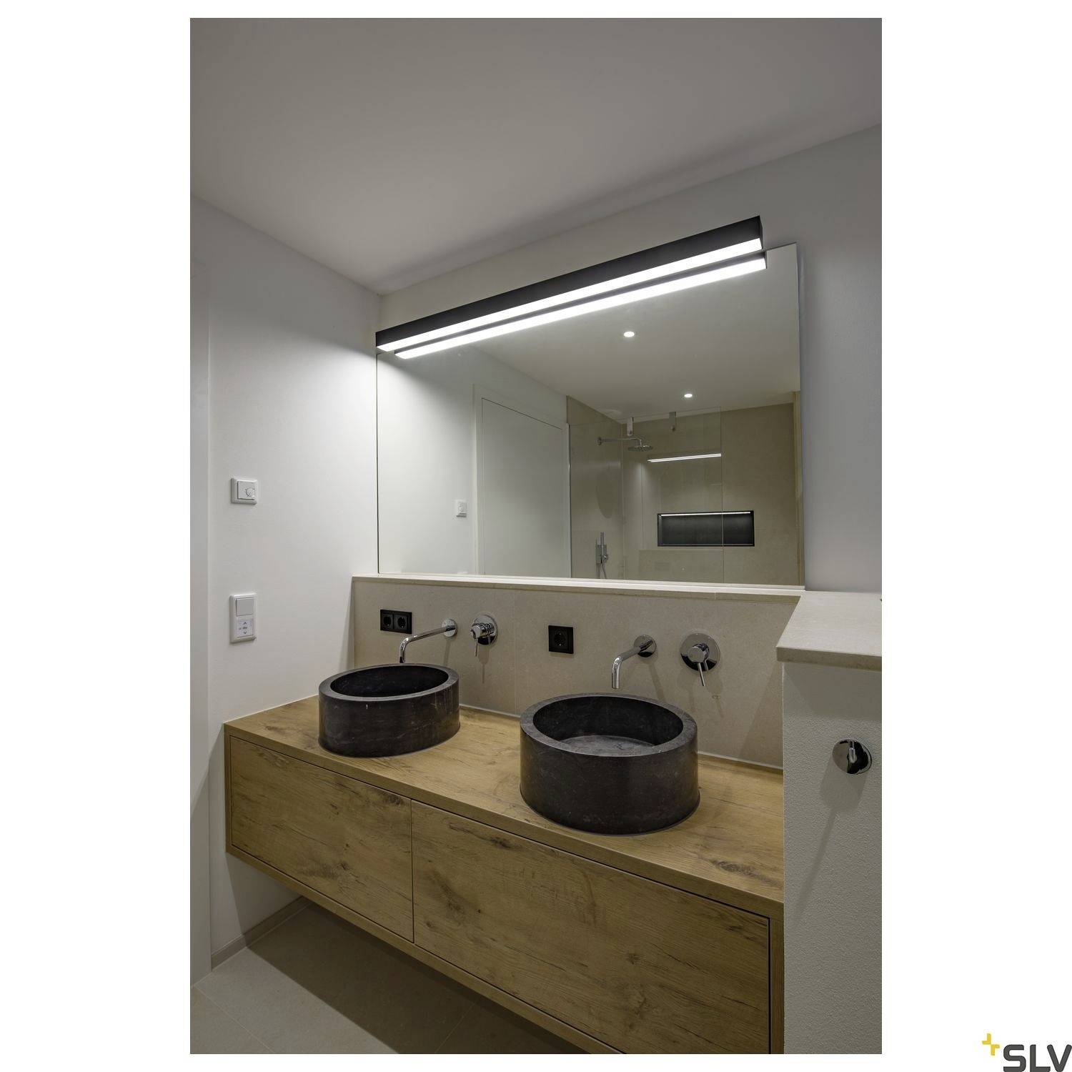 A modern bathroom with wooden furniture, two round washbasins and a large wall mirror; a stylish lighting element positioned above.
