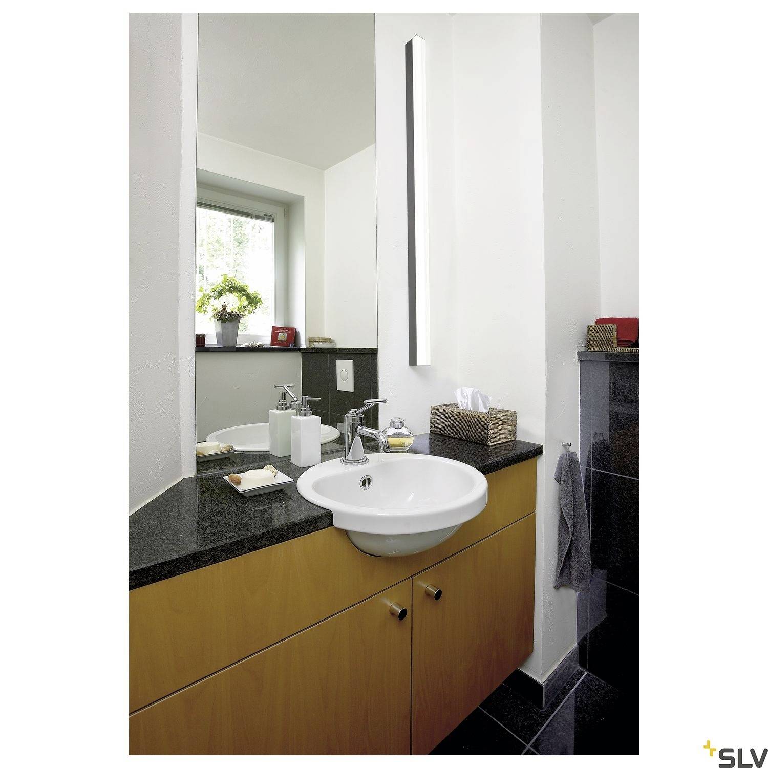 Bathroom with a washbasin, mirror and black granite worktop. In the corner, there is a window, with a plant beside it.