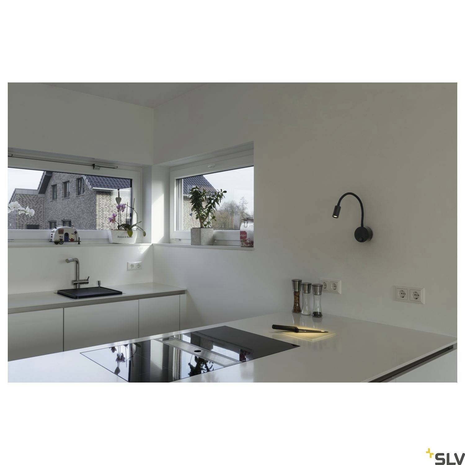 Modern kitchen with a central hob on an island. Large windows provide daylight, plants on the windowsill. Subtle wall light.