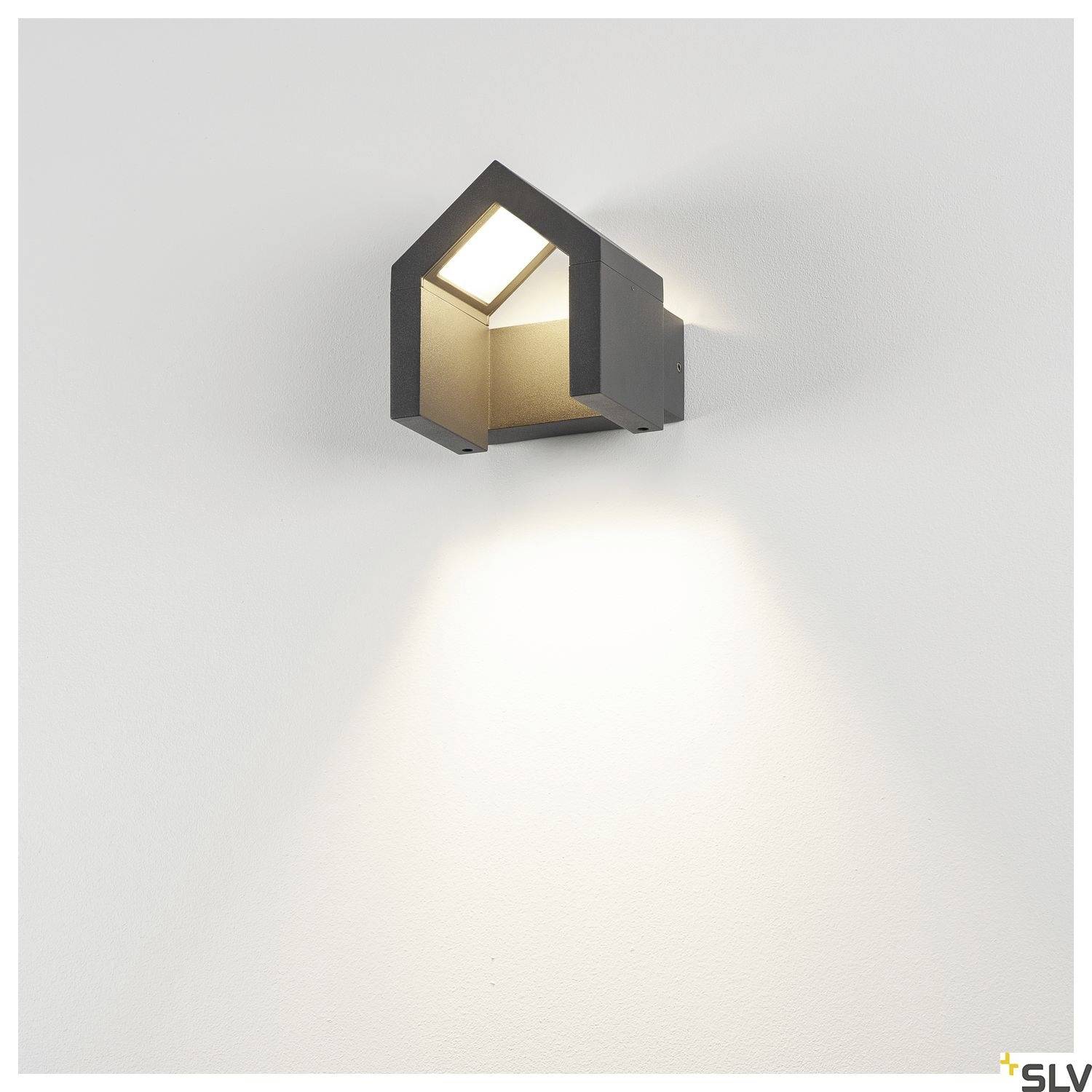 Wall light in the shape of a house emits bright light downwards, mounted on a white wall.