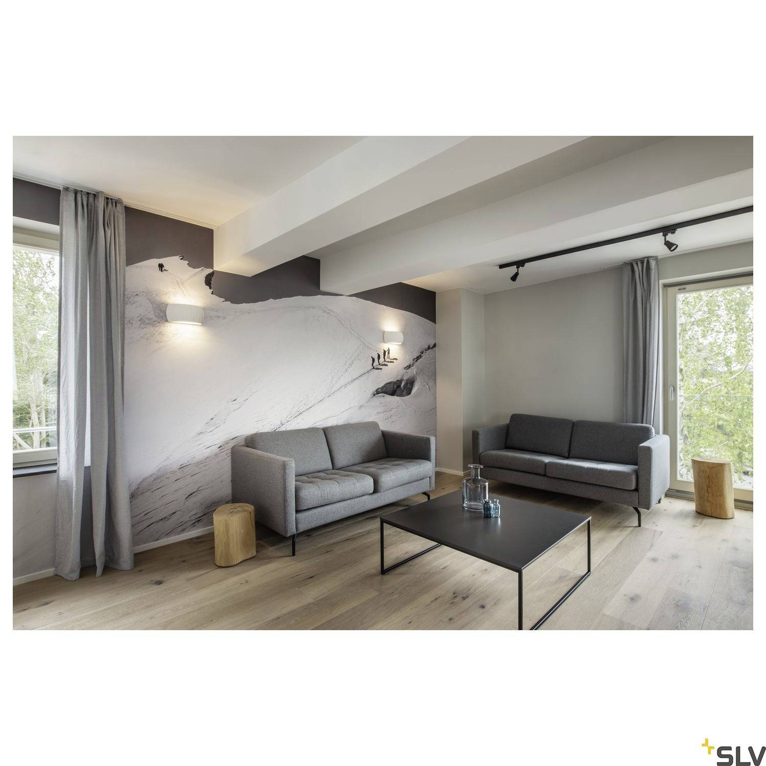 Living room with two grey sofas, wall painting of mountains, wooden flooring, glass and metal coffee table. Large windows with tree view.