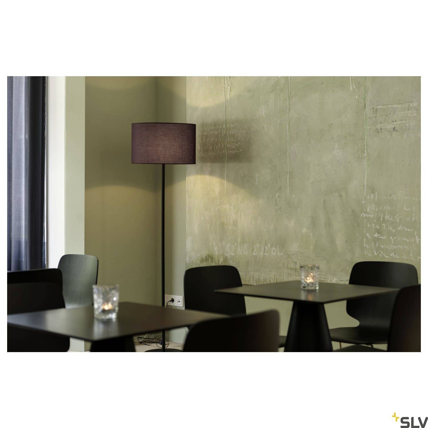 A cosy café with a standard lamp that provides soft lighting. Dark tables and candles on each table create a relaxed atmosphere.
