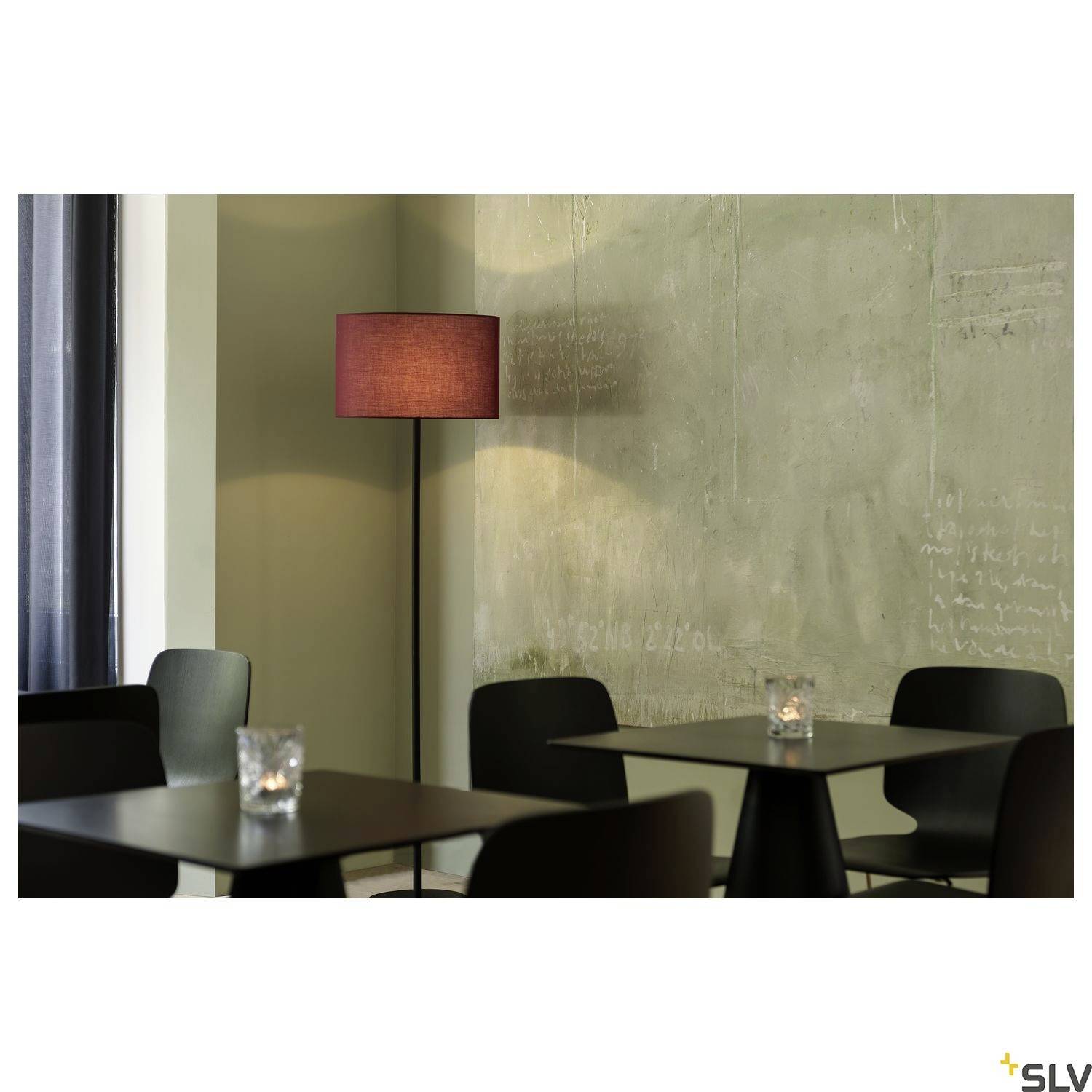 A modern-furnished café with black chairs and tables, illuminated by a standard lamp with a red shade against a grey wall.