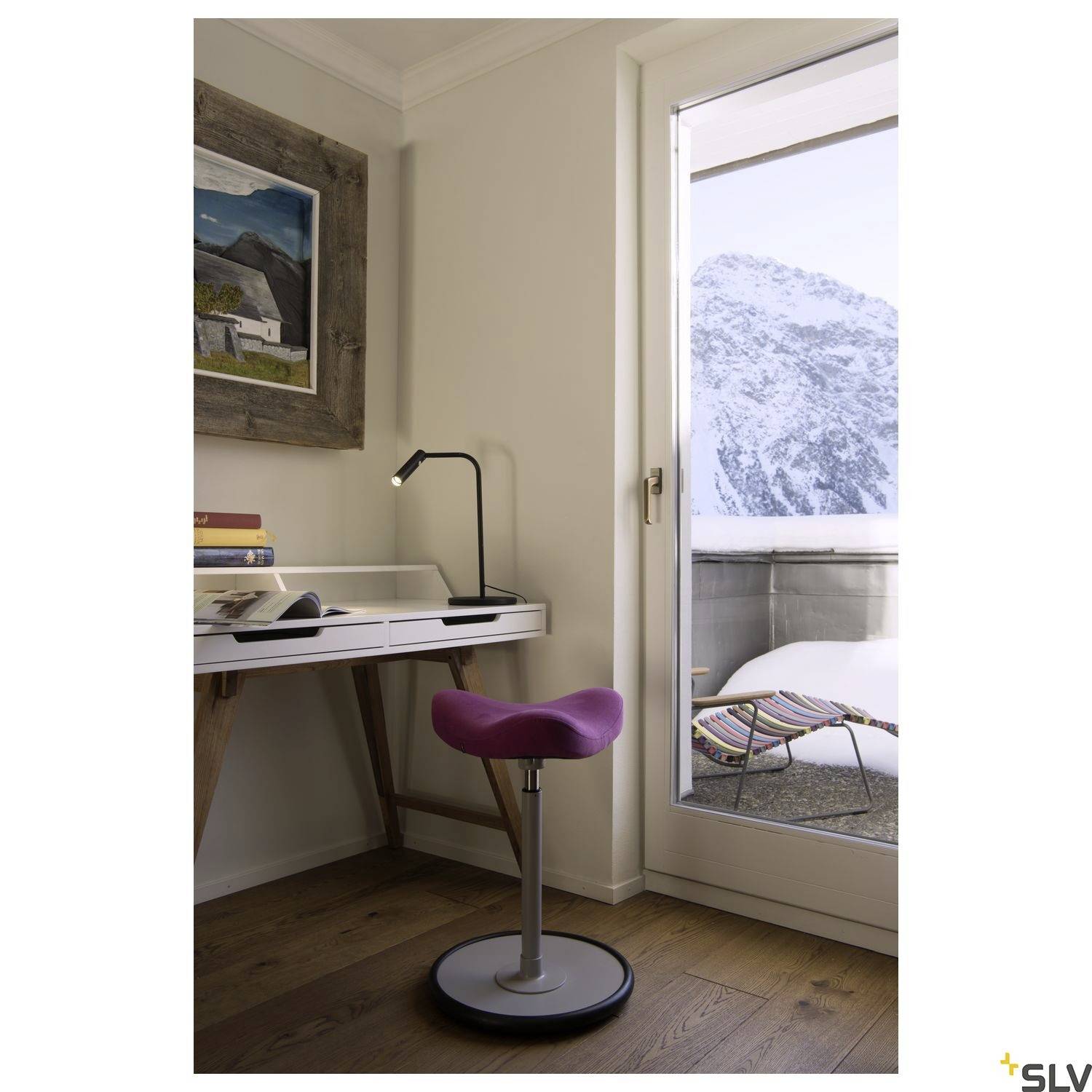 Workspace in a modern room with a view of snow-capped mountains. The desk has books and a lamp, with a red stool beside it.