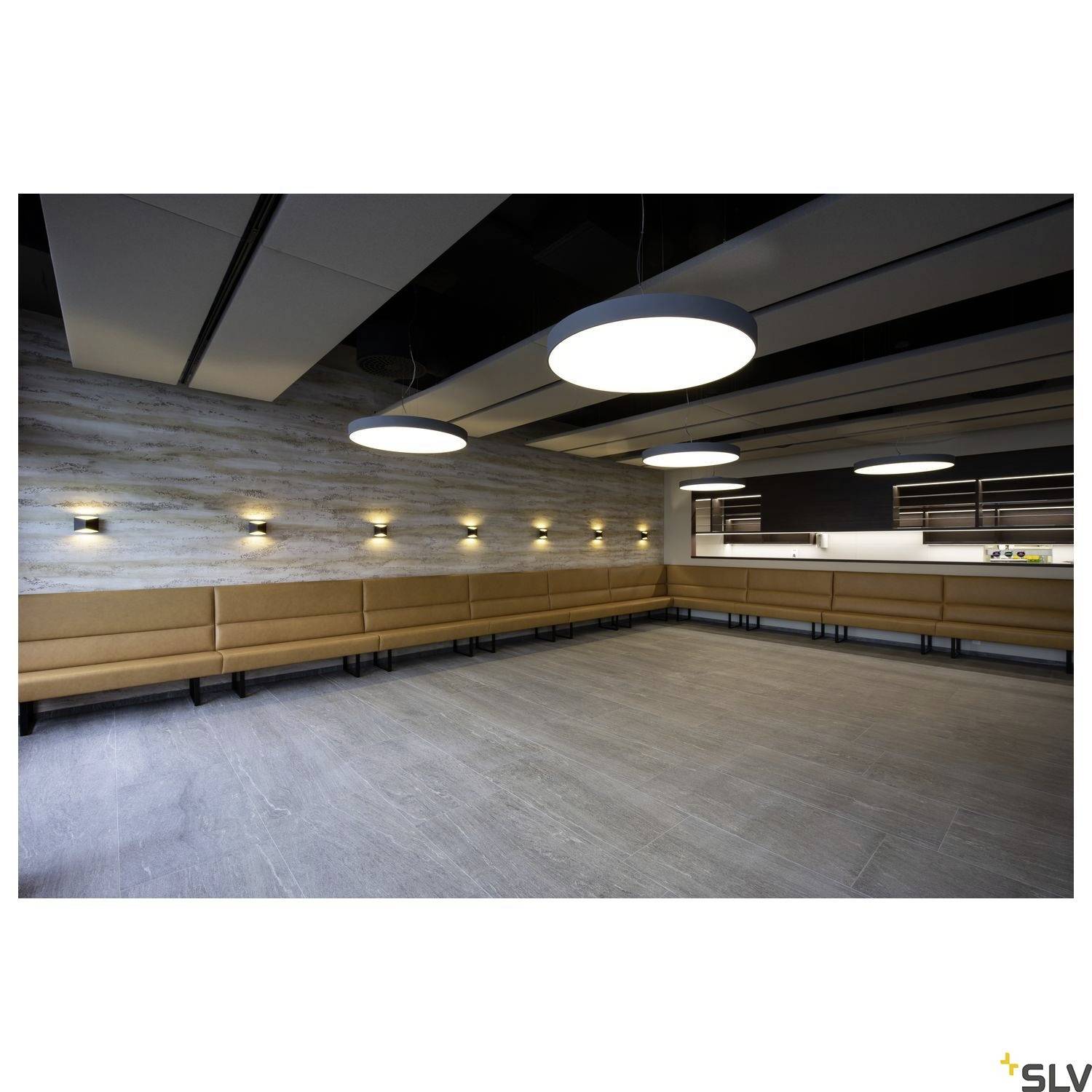 A modern, empty space with beige benches along the walls and large round ceiling lights. Walls made of grey wood.