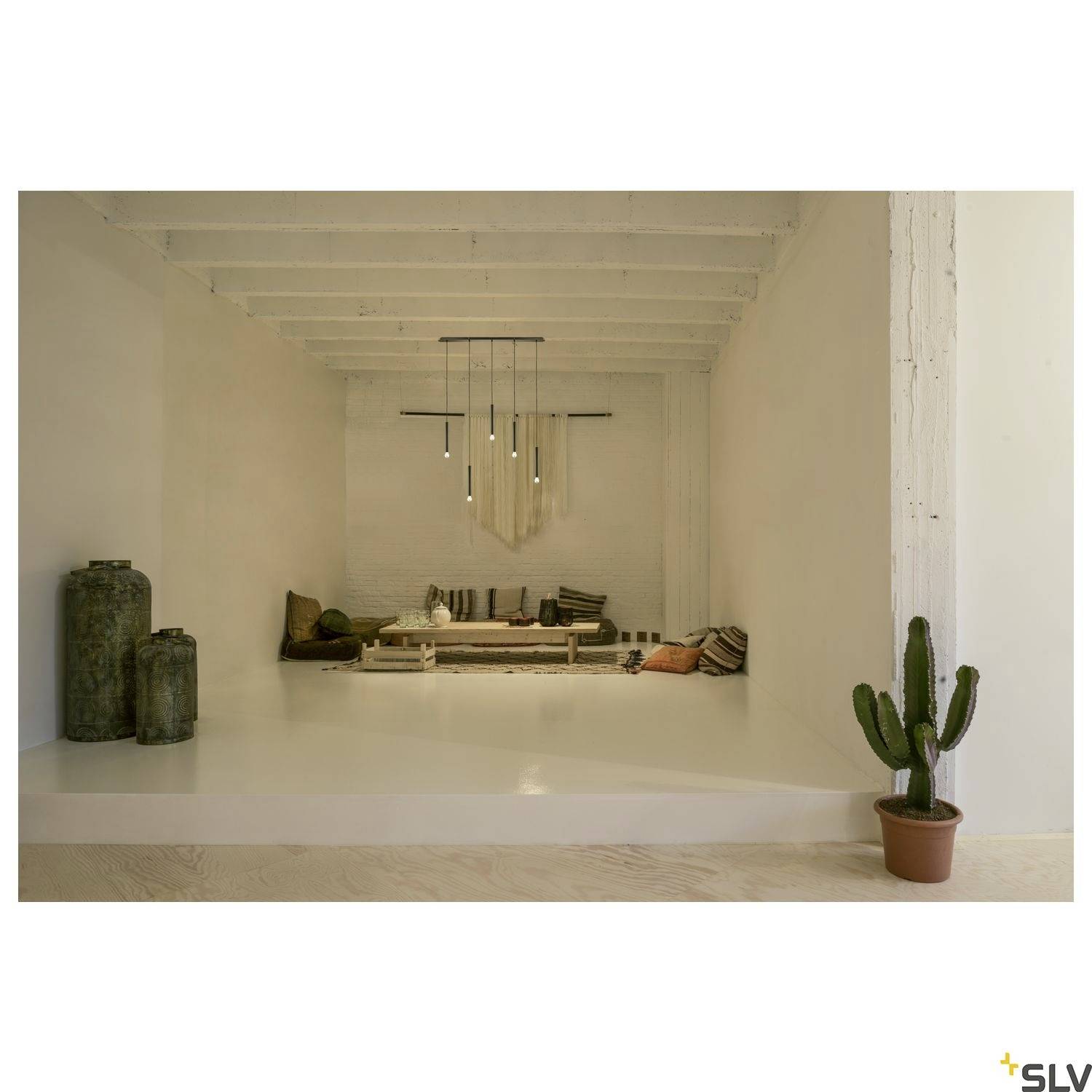 A minimalist living room with white furnishings, a cactus in a pot on the right, and two metal vases in the background on the left.