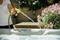 A person is pouring water into a hot tub using a garden hose. Pink blossoms can be seen in the background.