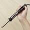 A hand is holding a soldering iron over a wooden table. The soldering iron has a black handle and a metal tip.