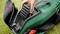 A hand is inserting a battery into a lawn mower. The lawn mower is green with a black casing.