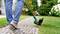A person is mowing grass along a paved path with an electric lawn trimmer in the garden.