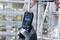 A person is holding a Bosch laser distance measure while measuring in an unfinished steel construction building for precise distance measurement.
