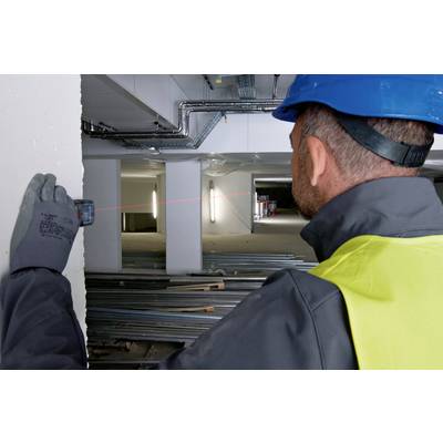 A construction worker wearing a hard hat and high-visibility vest is measuring the distance inside a building using a laser distance metre.
