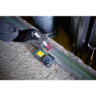 A person wearing gloves using a digital measuring instrument to measure the length of a metal beam in an industrial setting.