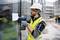 A construction worker wearing a hard hat and high-visibility vest is drilling a paper onto a glass wall at a building site.