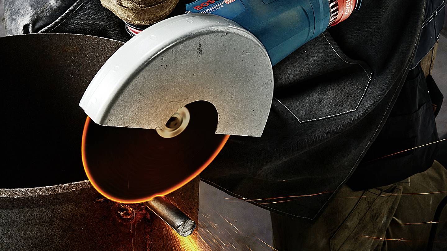 A person using an angle grinder to cut metal. Sparks fly from the cutting point and glow orange.