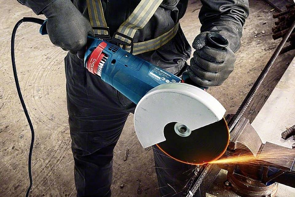 A worker is using an electric angle grinder to cut metal. Sparks are flying from the point of contact.
