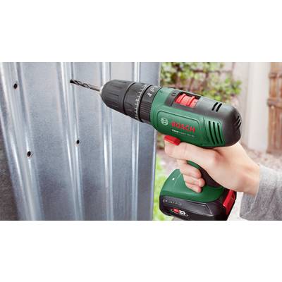 A hand is holding a Bosch cordless drill driver and drilling a hole in a metal sheet.