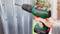 A hand is holding a Bosch cordless drill driver and drilling a hole in a metal sheet.