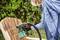 A person wearing protective clothing is spraying wooden slats of a chair with a paint spray gun outdoors.
