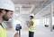 Construction workers in protective clothing use digital devices for surveying in an unfinished building. Modern construction planning and technology in action.