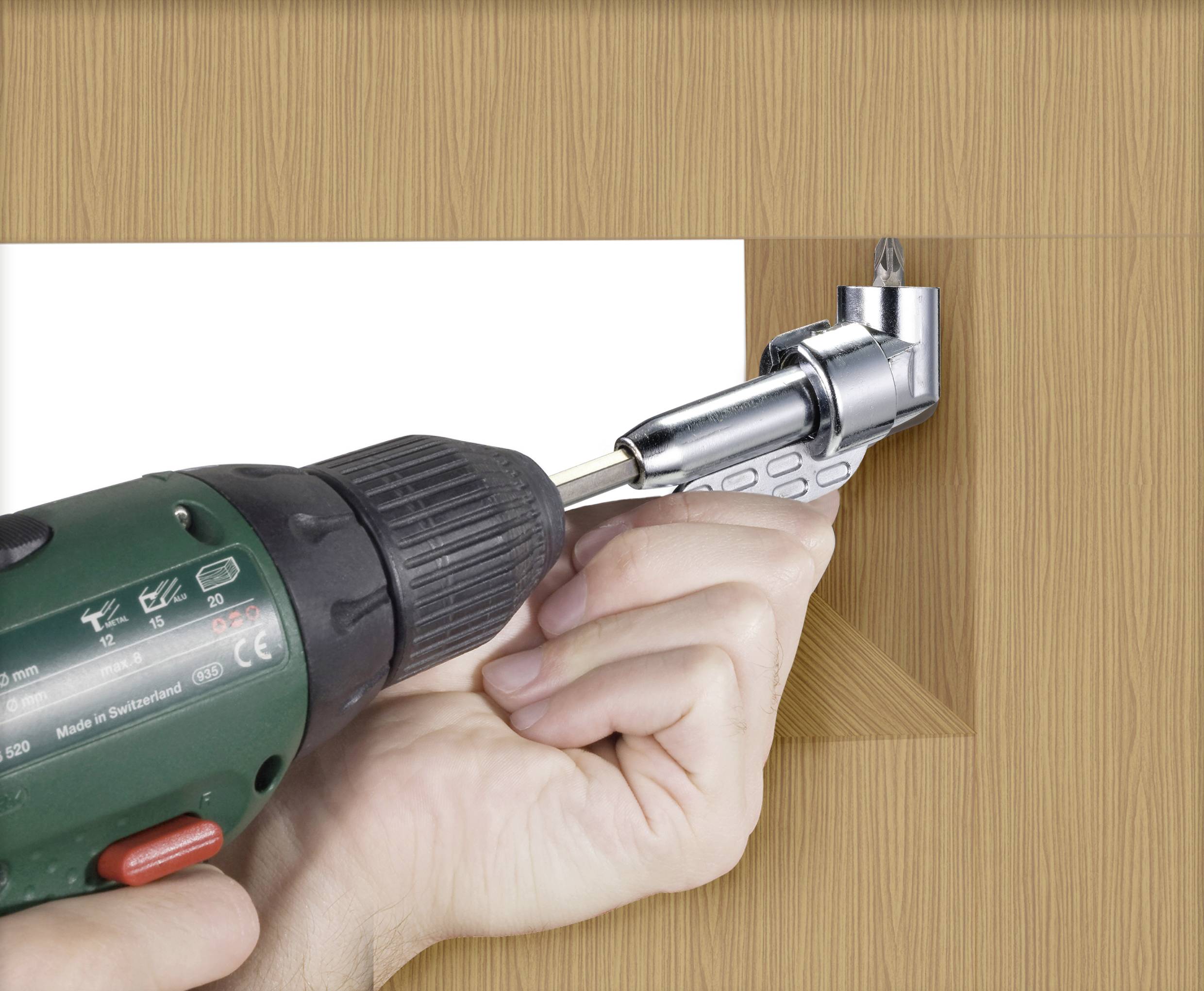 A hand is holding a drill and positioning an angle drill onto a wooden surface to drill a hole in a confined area.