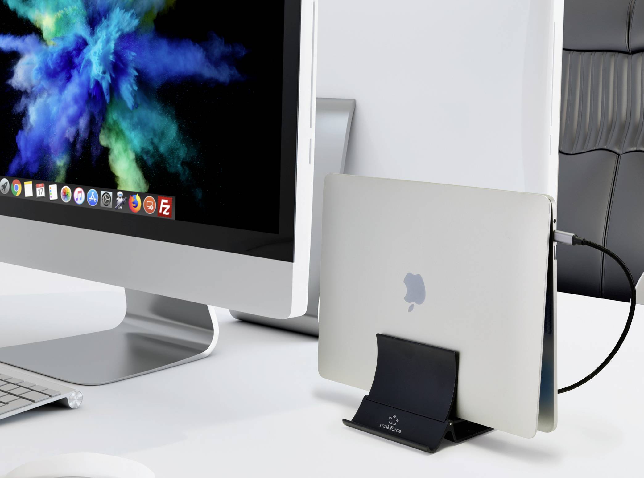 A computer screen displays colourful clouds. Beside it, a closed laptop sits in a vertical stand on a desk.