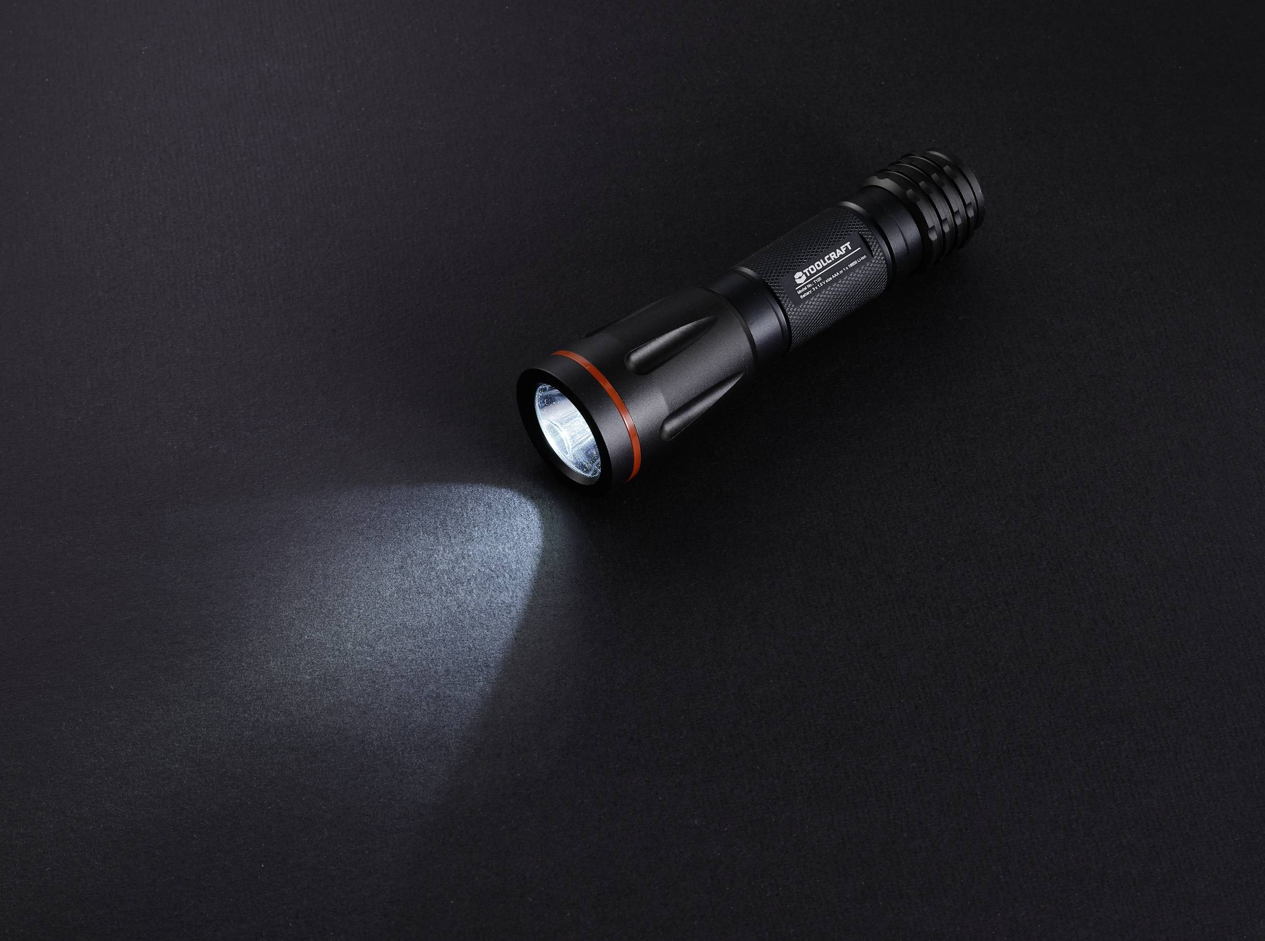 A black torch shines light onto a dark surface. It is positioned pointing to the left and is the only object in the image.