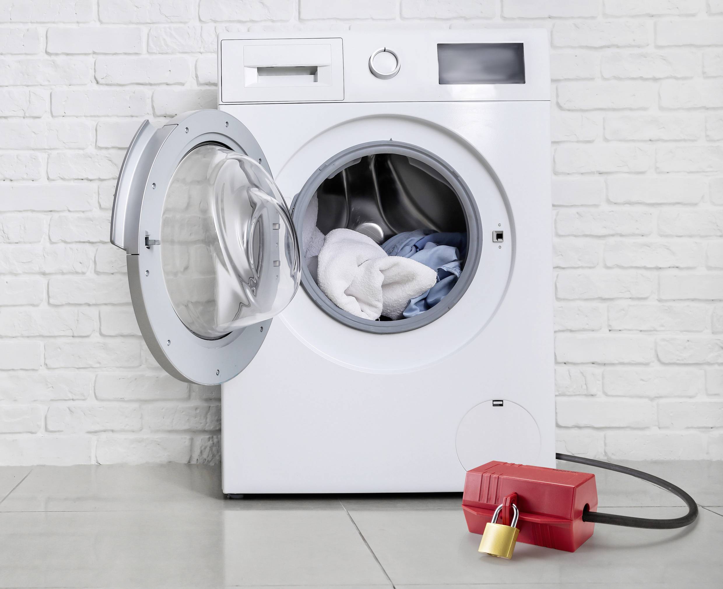 Washing machine with its door open, revealing laundry inside, with a red safety lock on the floor in front of it.