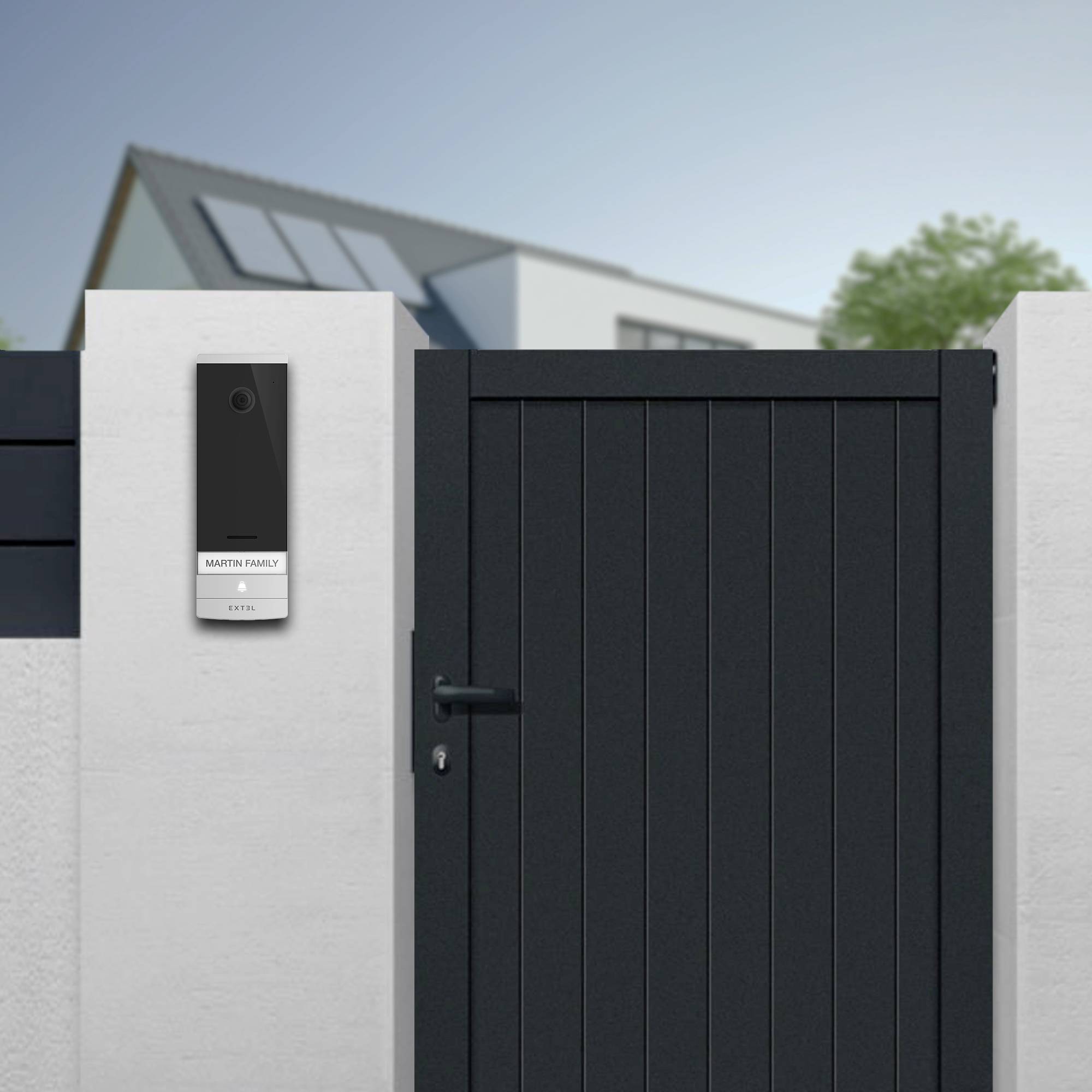 Metal gate with a modern intercom system next to a house. House number and family surname are displayed on the device.
