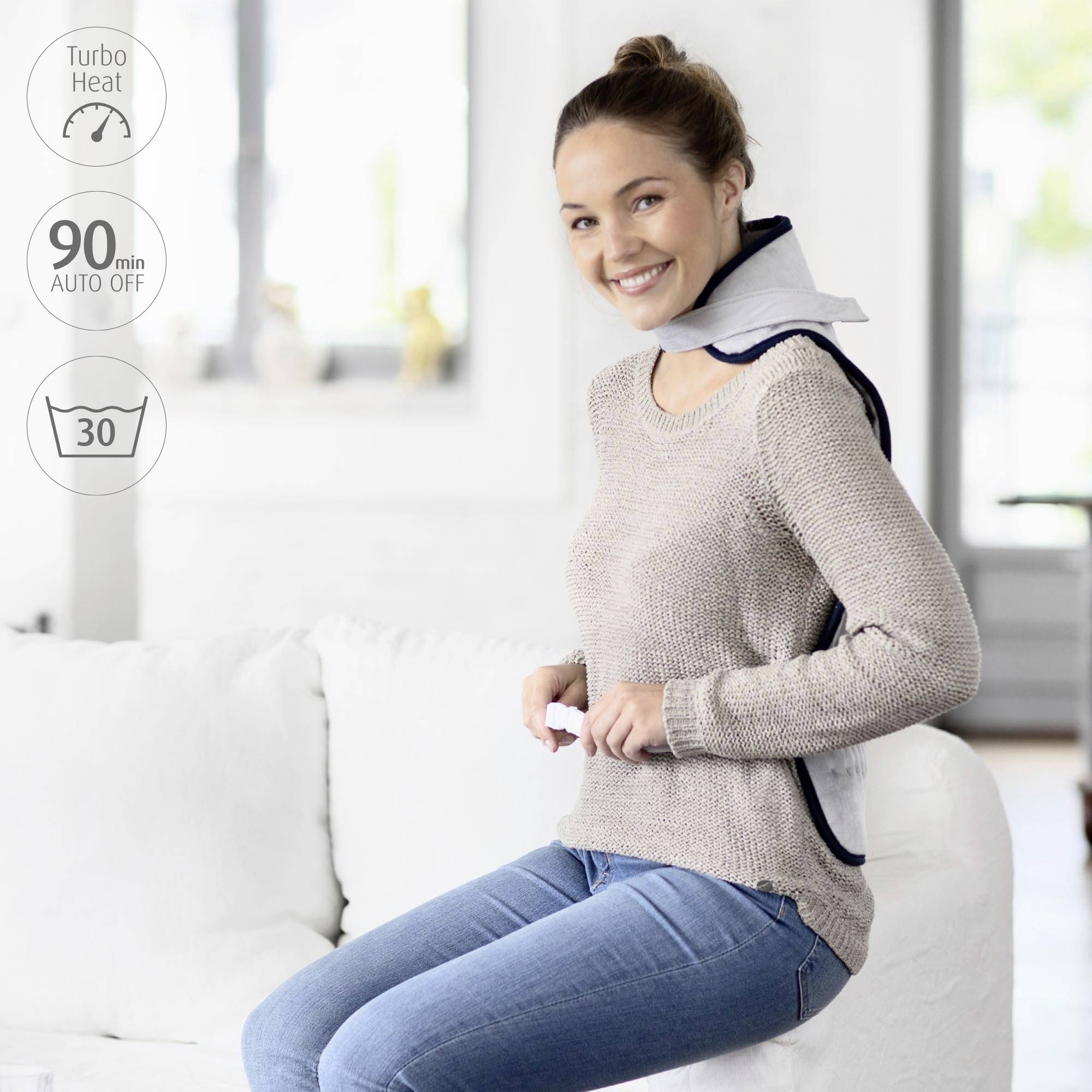 A woman sits on a sofa wearing a heating pad on her shoulders. Text: 'Turbo Heat', '90 min Auto Off', '30'. She smiles relaxedly.
