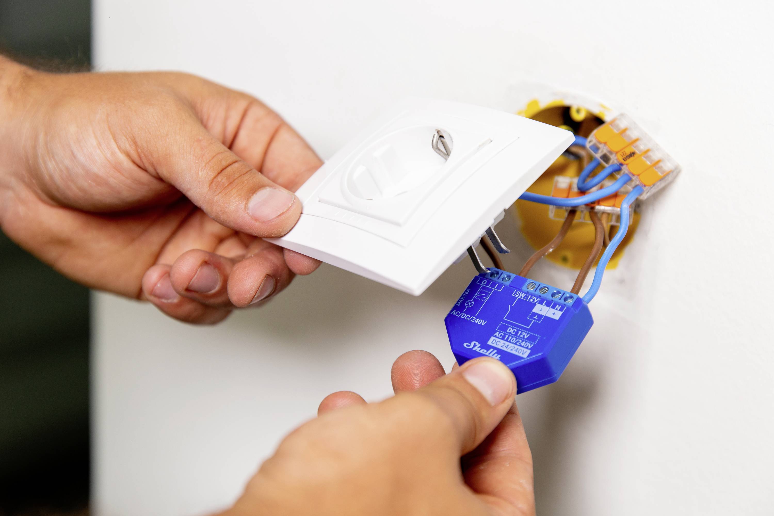 A person is installing a blue dimmer in a wall opening, connecting the cables to a remote light switch.