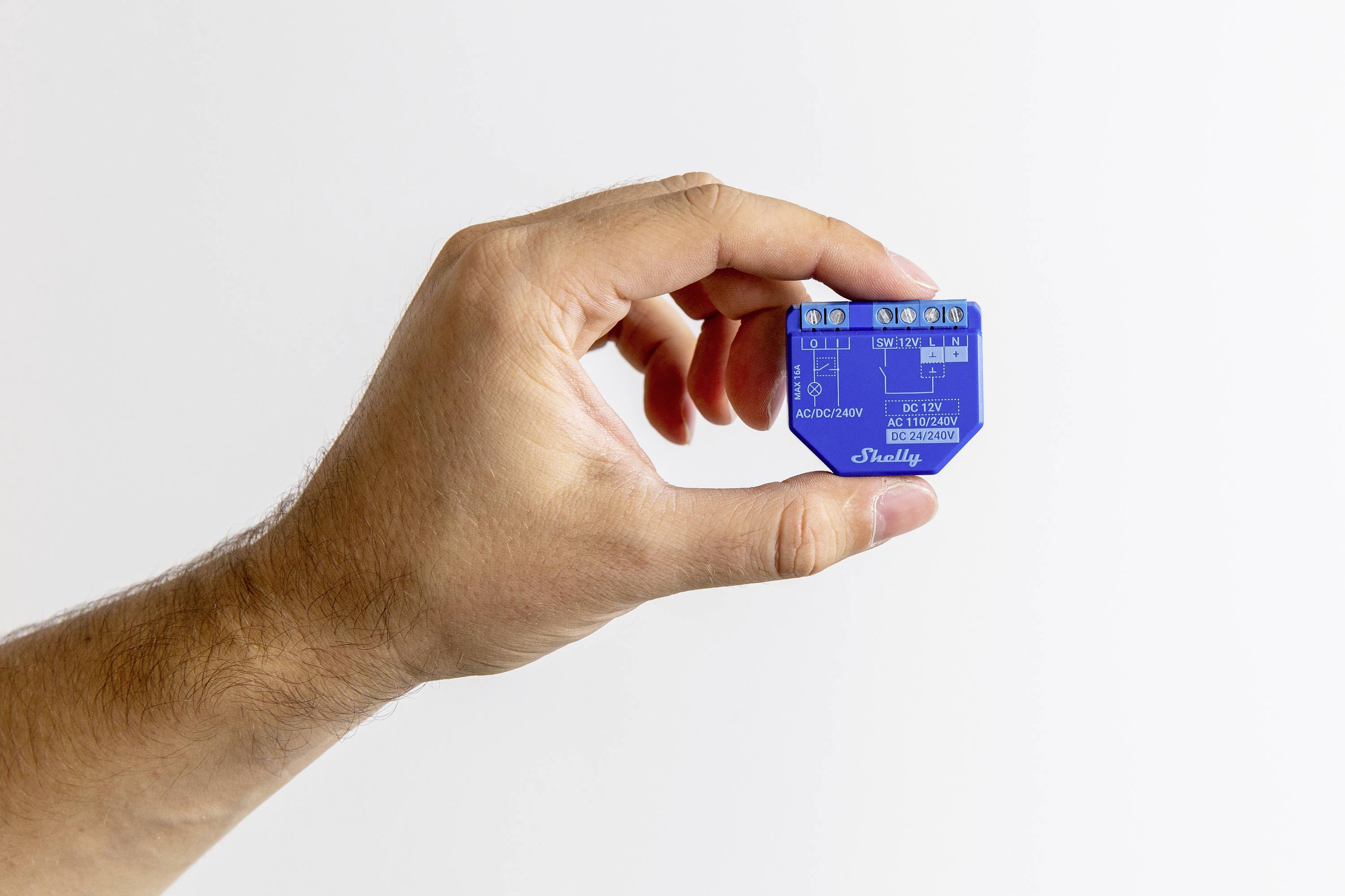 A hand is holding a small blue electronic component with connections and labels visible.