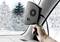 A hand is holding a portable car heater near the windscreen. Outside, snow-covered trees are visible.