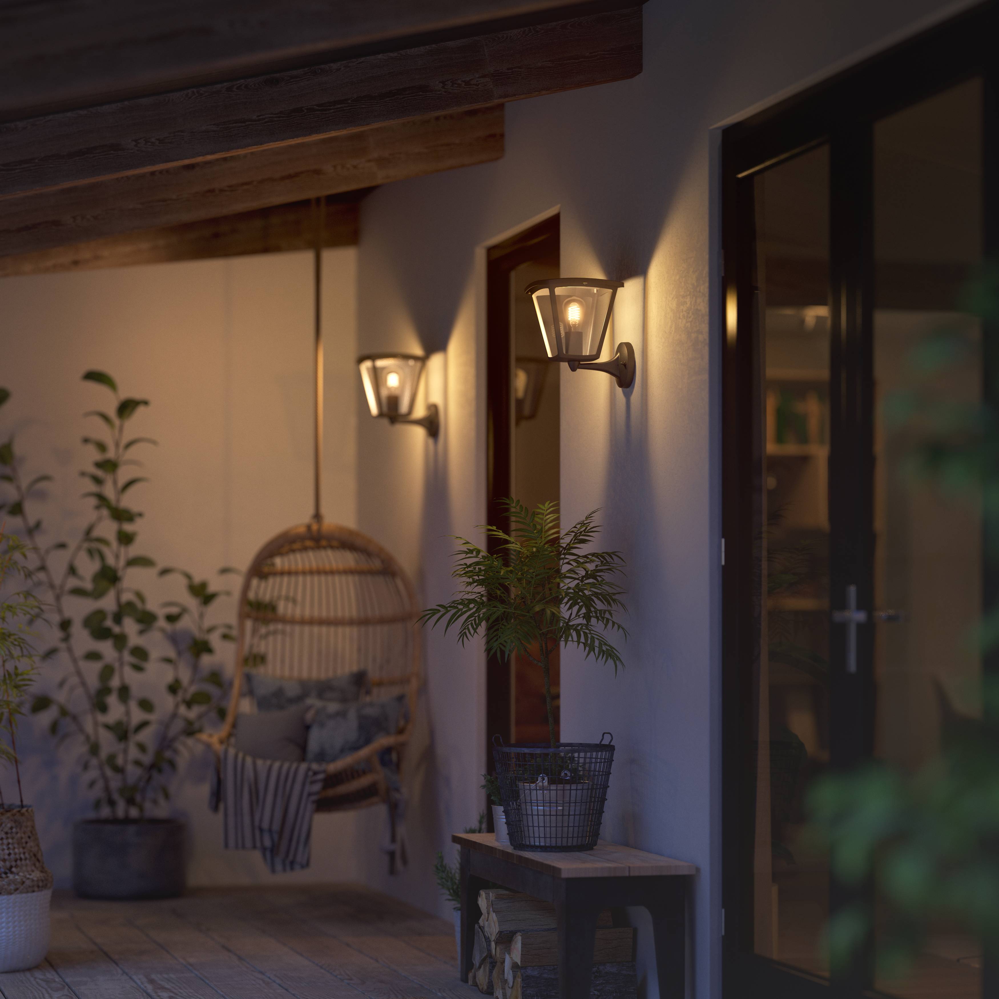 Illuminated terrace with a hanging chair, two wall-mounted lantern lamps, surrounded by plants and wooden flooring. Relaxed evening atmosphere.