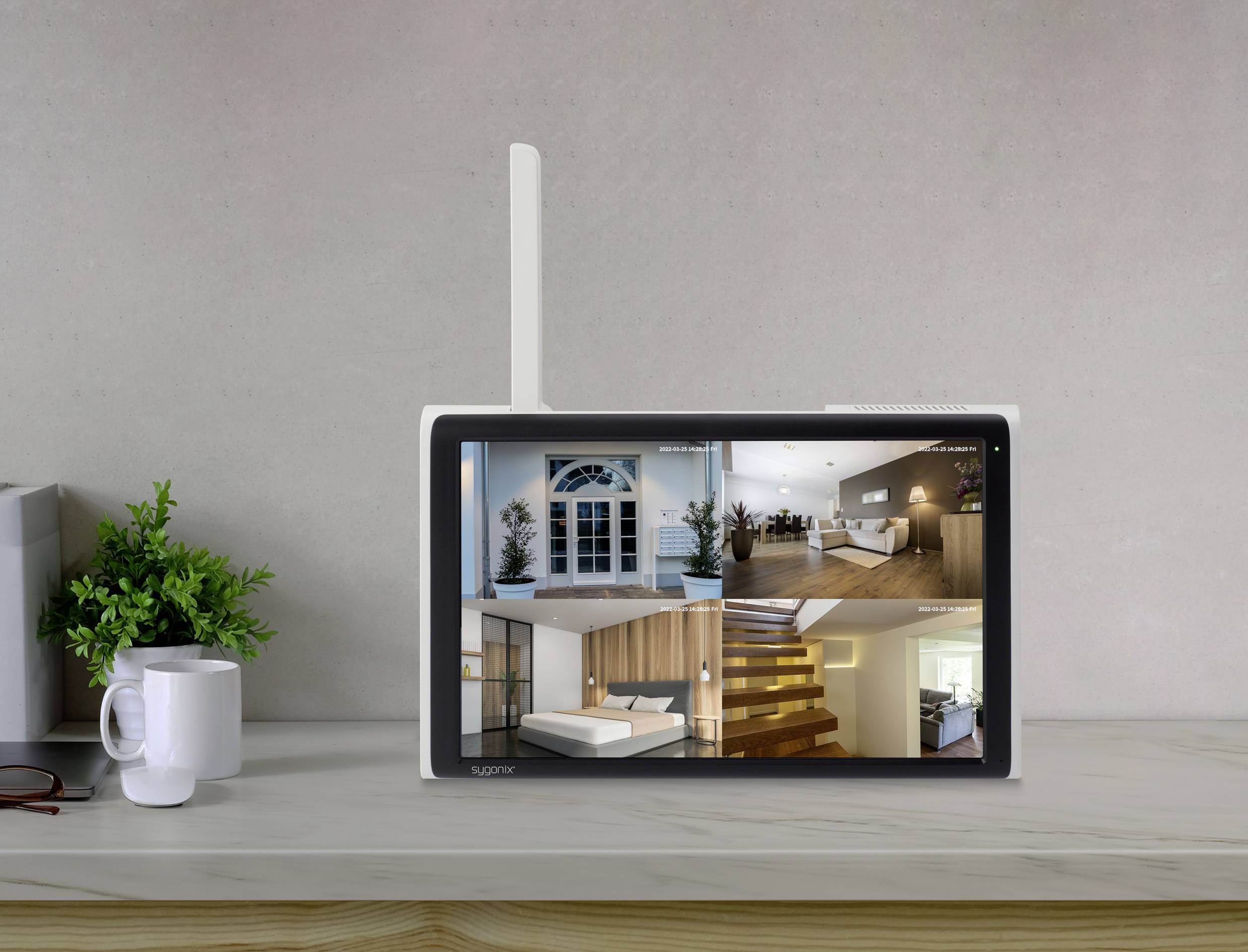 A monitor on a table displays security camera images of various rooms in a house. Next to it are a cup and a plant.