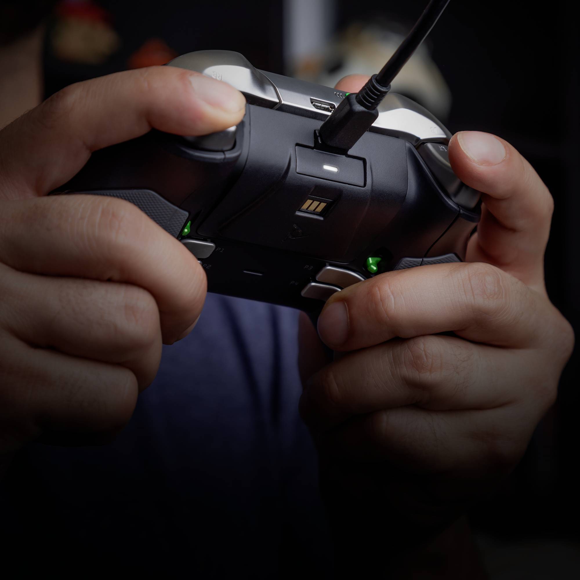 Hands holding a games controller connected to a cable, ready to play. Blurred objects are visible in the background.