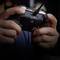 Hands holding a games controller connected to a cable, ready to play. Blurred objects are visible in the background.