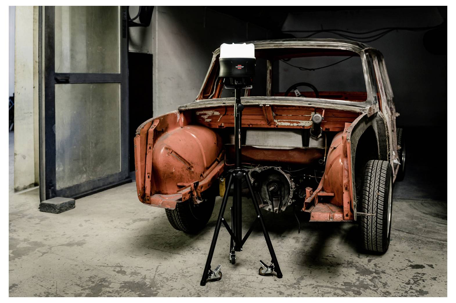 Partially restored vintage car body in a garage, with a tripod-mounted camera light positioned in front of it.