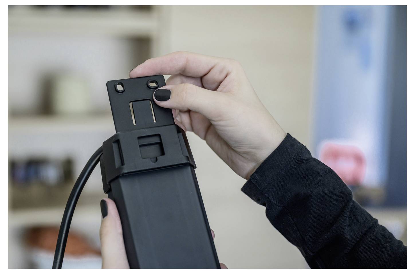 Close-up of a person adjusting a black device or appliance part with a cord, holding it with both hands indoors.
