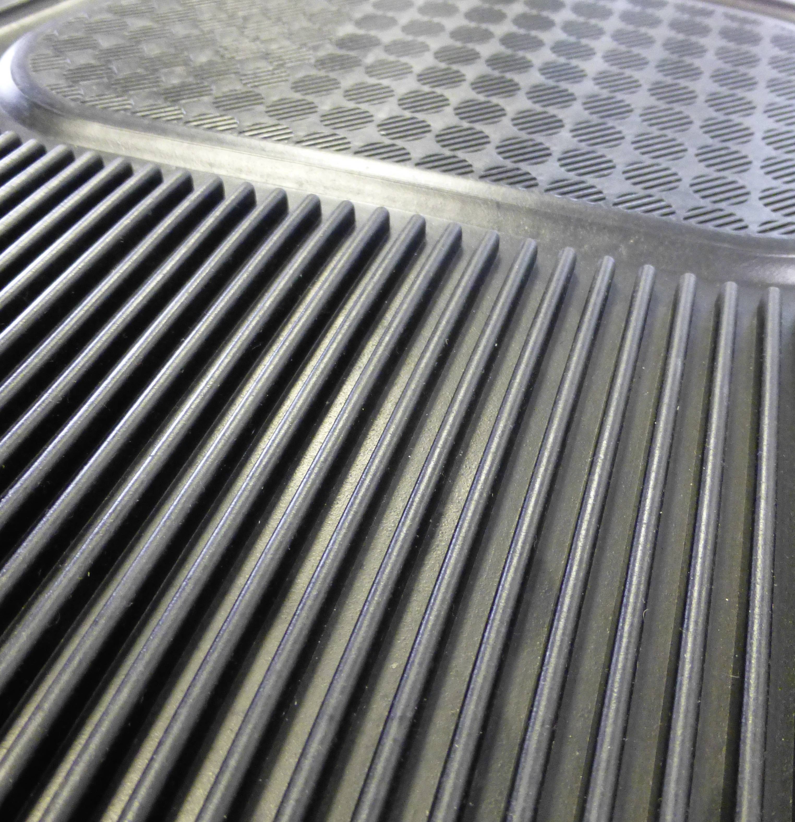 Close-up of a structured, ribbed surface made of black plastic, possibly a car mat, with a non-slip pattern.
