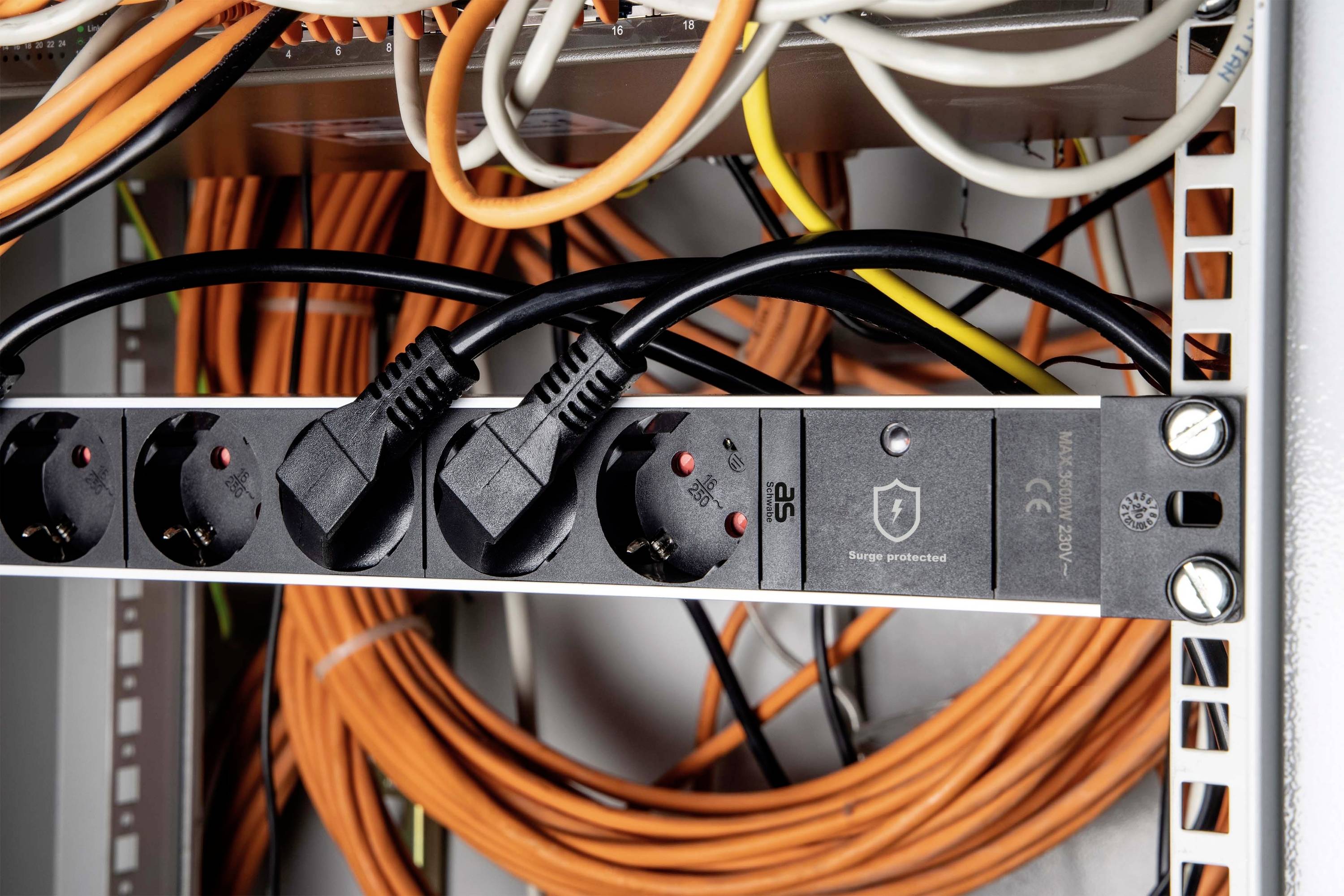An electronics cabinet with several orange cables and black plugs connected to a power strip.