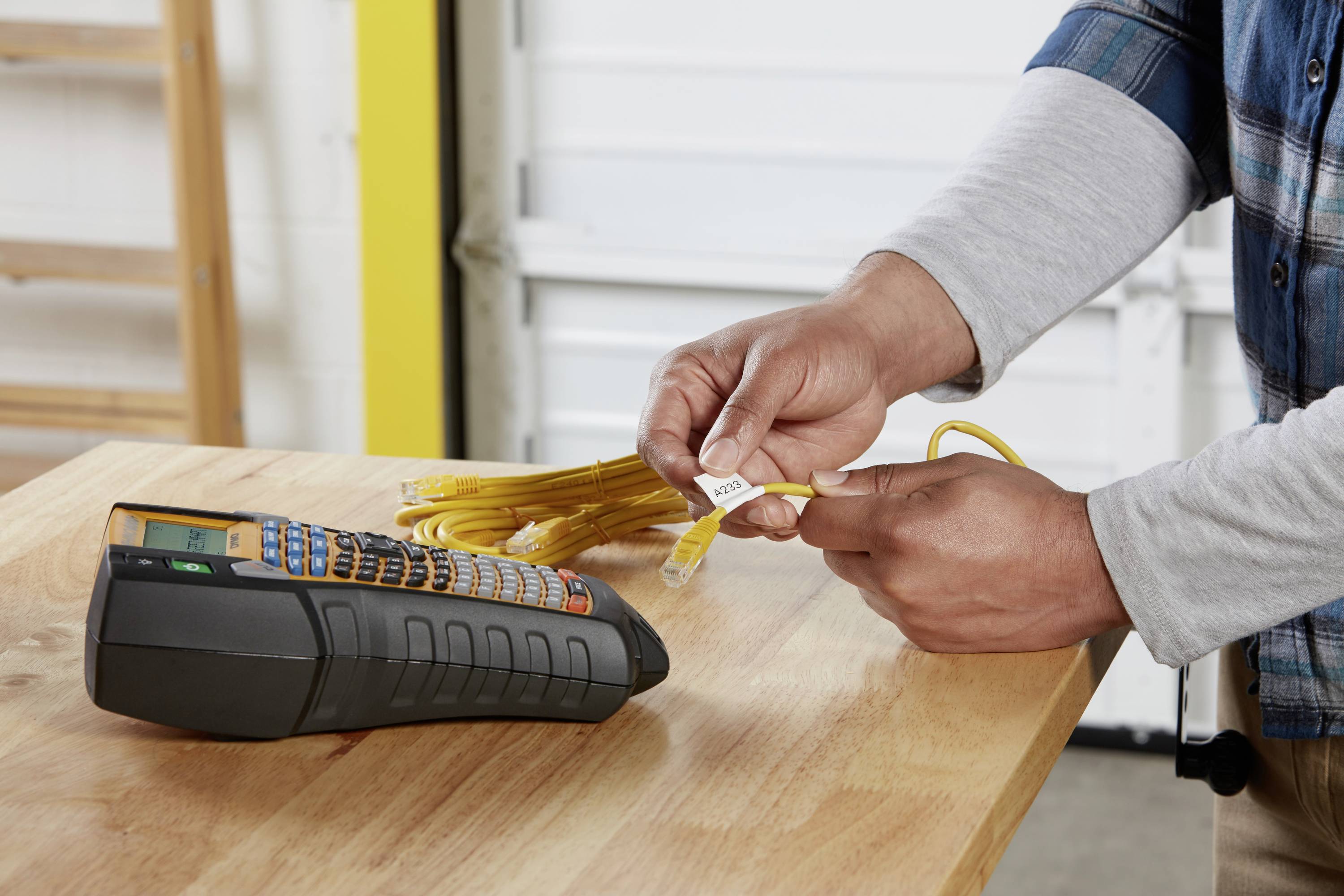 A person is holding a bundle of yellow network cables that are being labelled. A label printer sits on the table beside them.