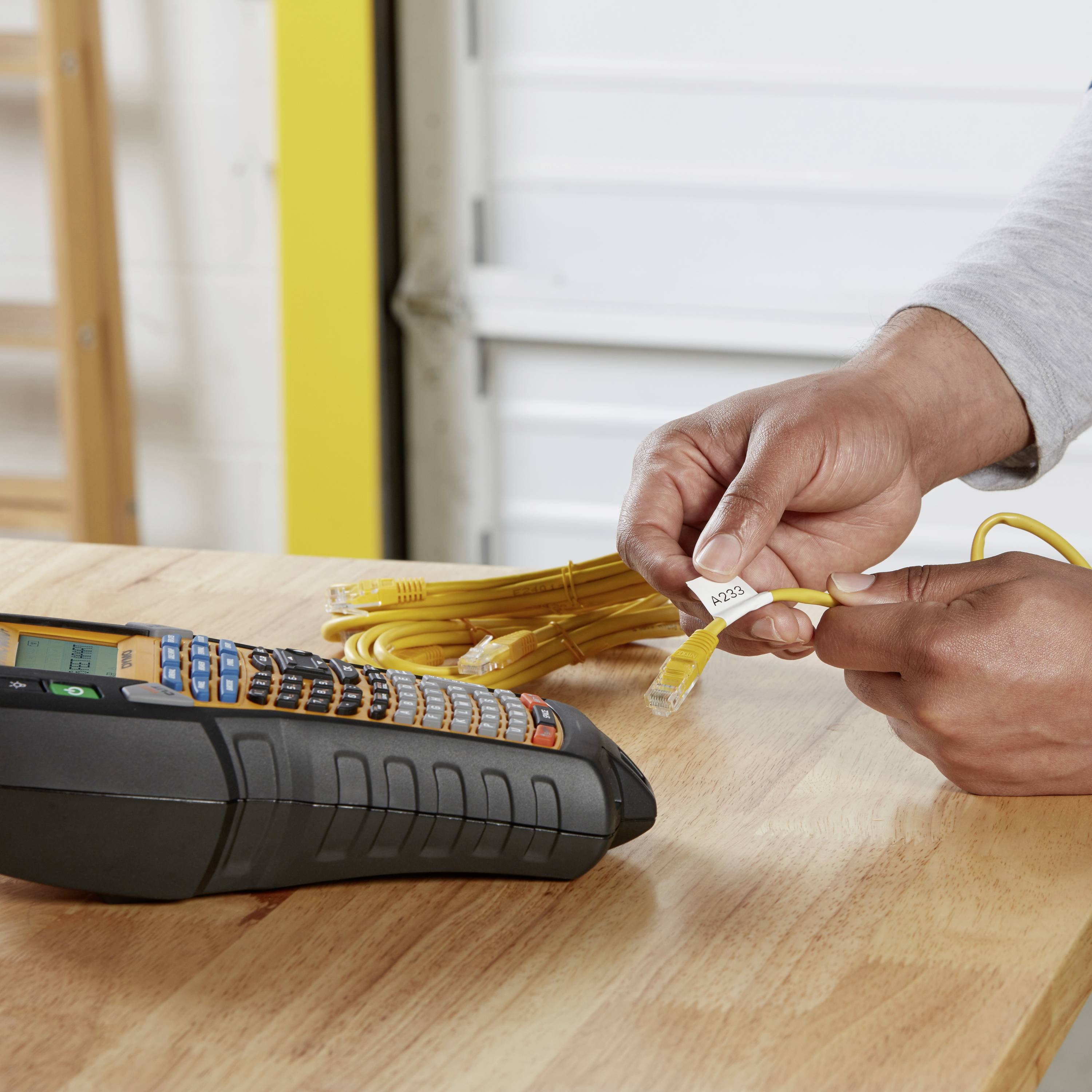 A hand is holding yellow network cables with a label. A measuring device is lying next to it on the table.
