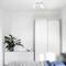 A minimalist bedroom with a white wardrobe, a chest of drawers with plants, and a bed with a grey blanket and blue pillow.