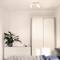 A simple bedroom with a white wardrobe, a chest of drawers, plants and a bed. Soft daylight illuminates the room.