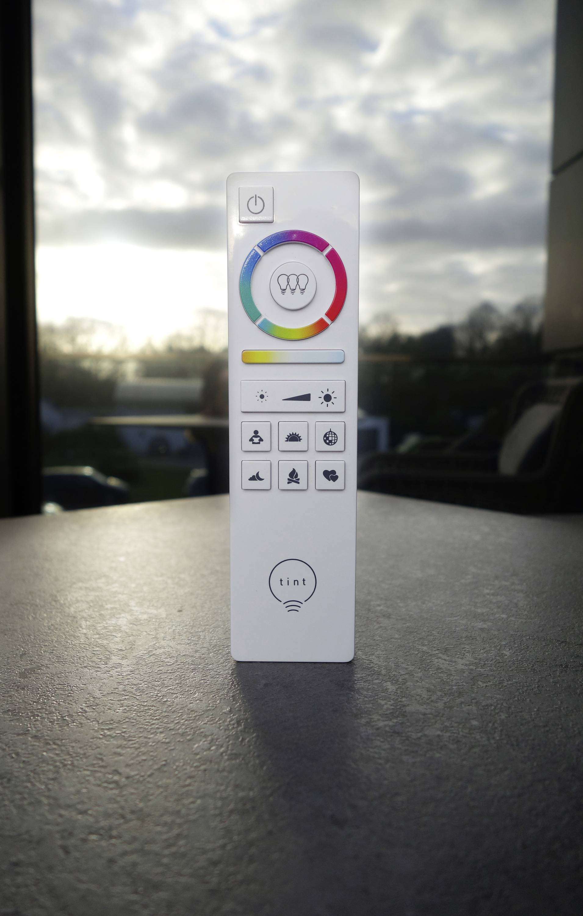 Remote control for intelligent lighting with a coloured ring and various buttons for light control near a window.